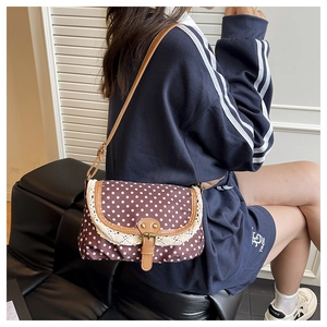 Close-up of vintage polka dot canvas bag with lace trim and brown leather strap on model