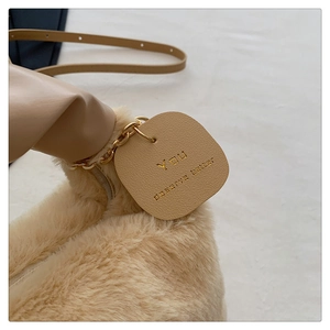 Détail d'un sac à main en peluche beige avec étiquette en cuir dorée et bandoulière fine