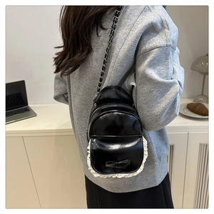 Detailansicht eines Minirucksacks aus schwarzem Lackleder mit weißer Spitze und Schleife