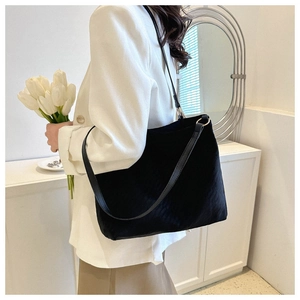 Side view of a black large capacity tote bag with long straps worn by a model in a modern room