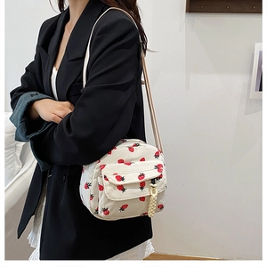 Detail of cream corduroy crossbody bag with strawberry print on a model in a black blazer