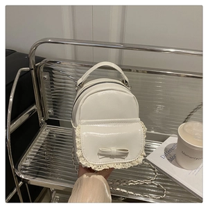 Nahaufnahme einer weißen Mini-Handtasche mit Spitzenbesatz, Schleife und Silberkette