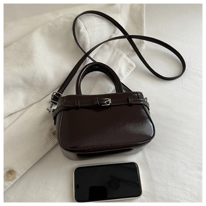 Macro shot of dark brown glossy leather bag with silver buckle on knit background