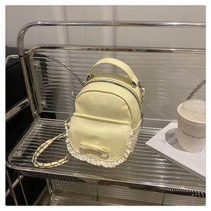 Detail der gelben Mini-Tasche mit weißem Spitzenbesatz, Schleife und Kettenriemen