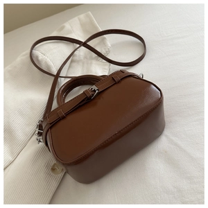 Detailed close-up of brown faux leather handbag with metal buckle and oil-wax texture