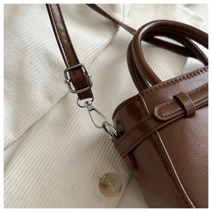 Detailed view of dark brown leather handbag featuring silver metal buckles and straps