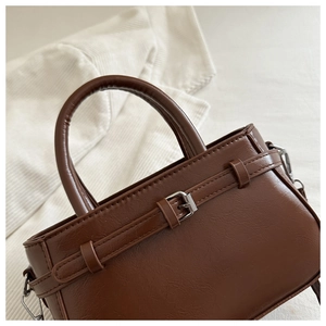 Close-up of brown leather handbag featuring silver metal buckle and lychee texture