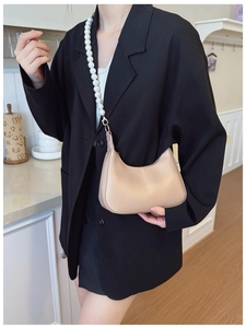 Detail of beige crescent underarm bag featuring a decorative large pearl shoulder strap