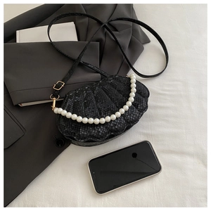 Detail of black shell-shaped bag with faux snakeskin texture and pearl handle accessory
