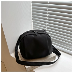 Close-up of black nylon shell crossbody bag with dual zippers on a minimalist backdrop
