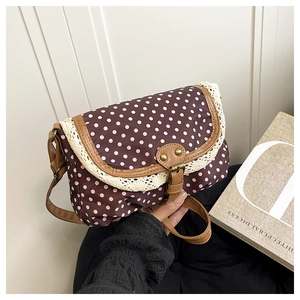 Detail of brown polka dot shoulder bag with lace trim and leather strap held by a model