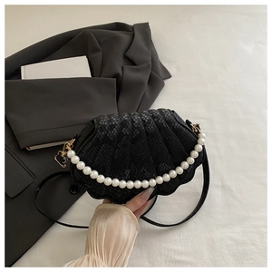 Detail of black shell-shaped bag featuring snake skin texture and oversized pearl handle