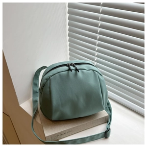 Close-up of a teal crescent crossbody bag with black dual zippers on minimalist props