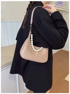 Detail of beige crescent shoulder bag featuring pearl chain and golden text