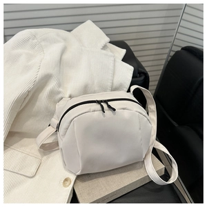 Detail of a minimalist cream crescent crossbody bag with double zippers on a book