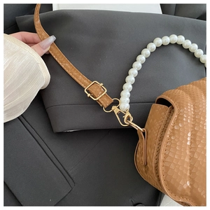 Detail of embossed brown leather bag featuring faux pearl chain and gold metal hardware