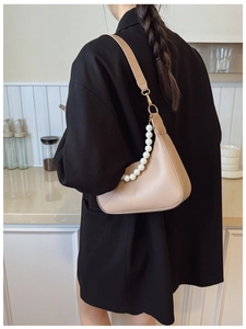Detailed view of the beige crescent bag with large pearl strap and gold brand lettering