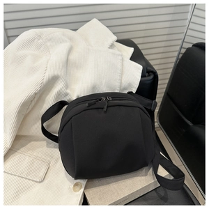 Close-up of black crossbody shell bag with dual zippers on a white corduroy jacket