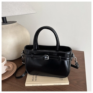 Gros plan d'un sac à main noir en similicuir brillant avec boucle en métal chic