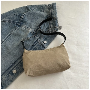 Close-up of khaki pleated fabric bag with silver chain detail on denim background