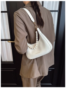 Close-up of white half-moon shoulder bag with elegant pearl strap and gold lettering