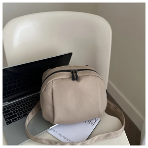 Vue détaillée d'un sac bandoulière en nylon beige sur une chaise avec PC et magazine