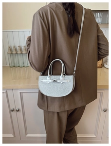 Detail showing a silver glitter crescent handbag with a sleek metallic clasp and leather strap