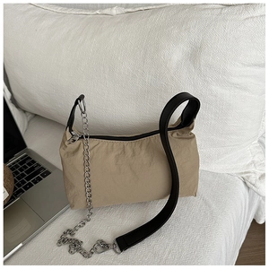 Close-up of beige nylon shoulder bag with silver chain detail and black strap on bed