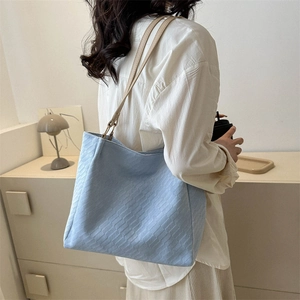 Light blue woven tote bag with leather straps worn by model in a minimalist setting