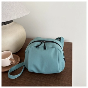 Detail of mint green crossbody shell bag with double black zippers on a wooden table