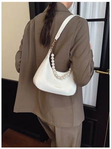 White crescent underarm bag with large pearl strap detail and gold lettering on the front