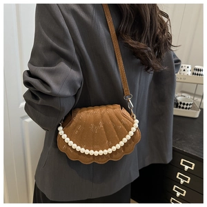 Detail of a brown shell-shaped bag with lizard texture and pearl chain on a grey blazer