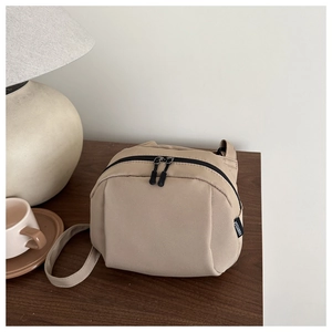 Detail of khaki nylon crossbody bag on wooden table with a coffee cup and lamp