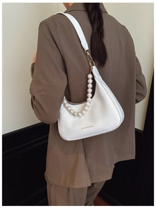 Close-up of white crescent bag with large pearl strap detail on a brown blazer outfit