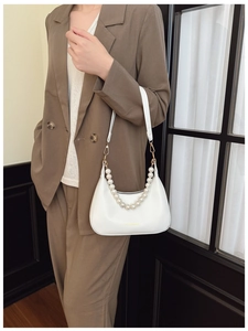 Chic white crescent bag with oversized pearl chain detail on stylish brown blazer