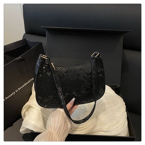 Detail of black snakeskin texture shoulder bag with gold hardware on silk background