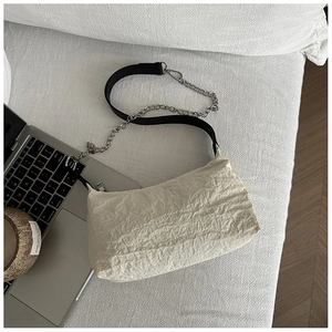 Detail of cream pleated fabric shoulder bag with black strap and silver chain accent