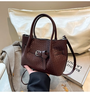 Detailed close-up of dark coffee woven handbag with circular handles and leather buckle