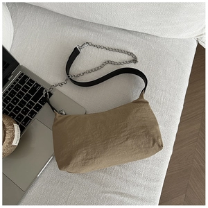Close-up of khaki nylon shoulder bag with leather chain strap on a white sofa