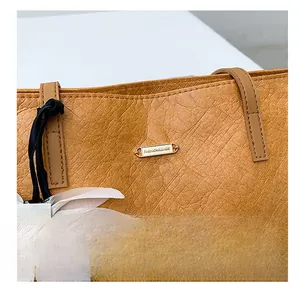 Detailansicht der braunen Tragetasche aus genarbtem Leder mit goldenem Logo
