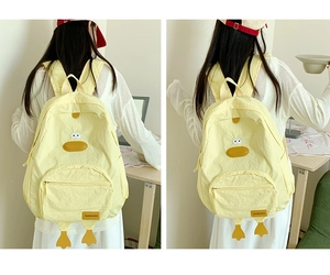 Detail view of yellow canvas backpack with cute cartoon duck design and fashion tag