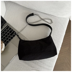 Minimalist black crescent crossbody bag with silver chain strap on a white sofa