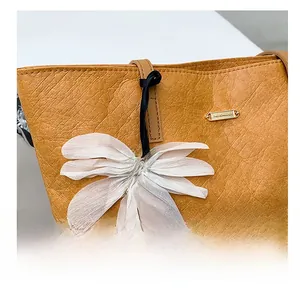 Detail der senfgelben Tragetasche mit Lederstruktur und dekorativem Blumenanhänger