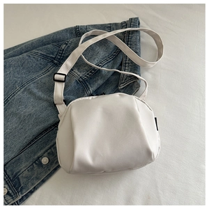Close-up of a white padded nylon cloud bag with an adjustable strap on a denim jacket