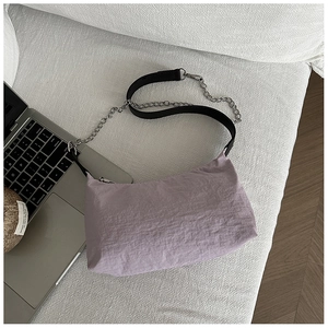 Detail view of lavender pleated nylon shoulder bag with silver chain strap on white fabric