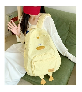 Close-up of yellow cartoon duck backpack with FASHION & BAGS tag on green sofa