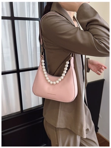 Detail of pink crescent bag with elegant pearl chain handle worn over a khaki suit
