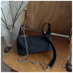Detail of black nylon tote with wide faux leather strap and silver chain on a wooden chair