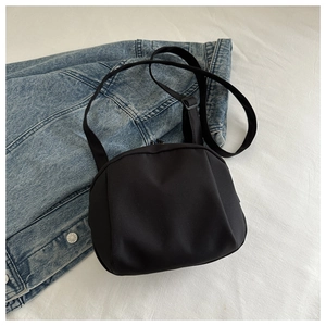 Detail view of a black nylon shell chest bag on denim and white textured fabric