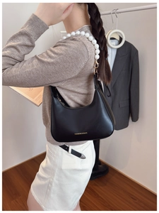 Dettaglio borsa hobo in pelle nera con manico in perle bianche e fibbie in metallo dorato